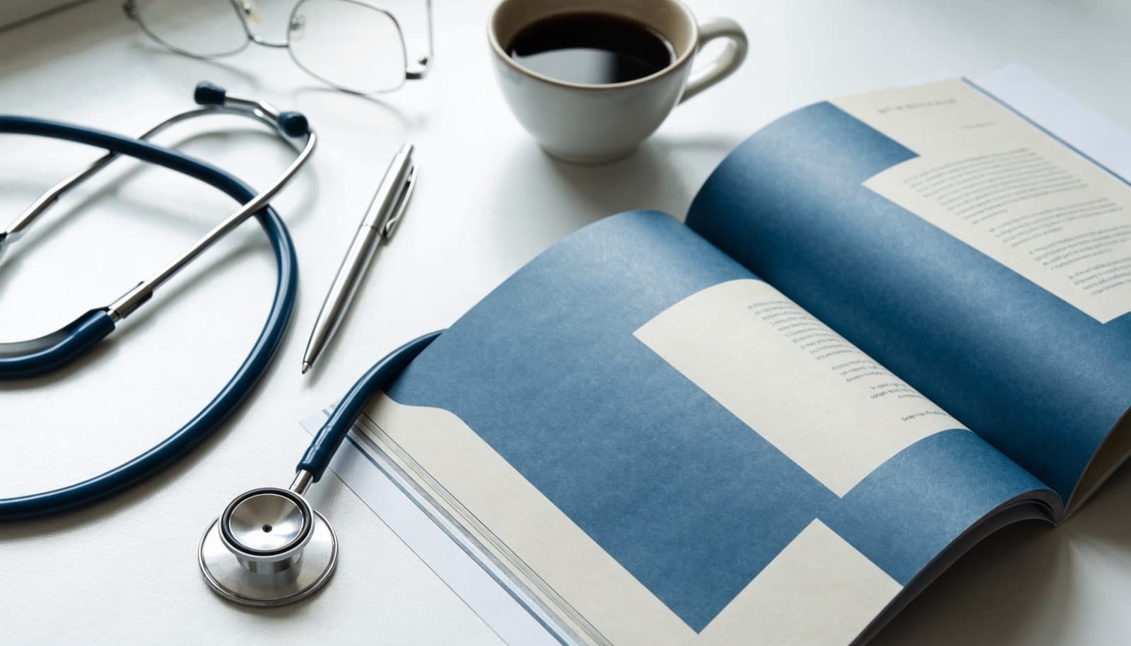 An open clinical guideline booklet on a desk beside a stethoscope, glasses, a pen and a cup of coffee